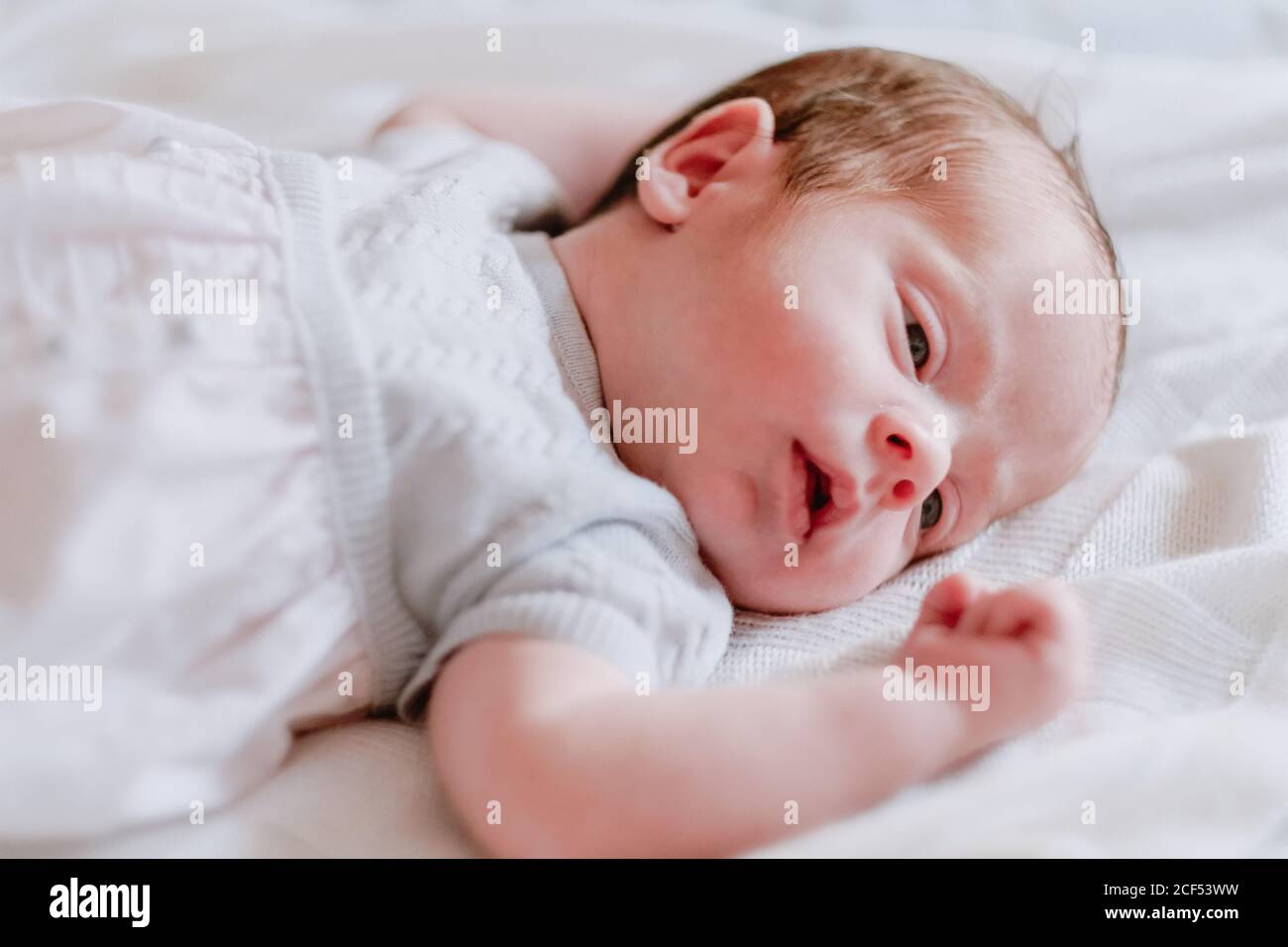 From above of cute tiny newborn baby in white bodysuit sleeping peacefully on black background Stock Photo