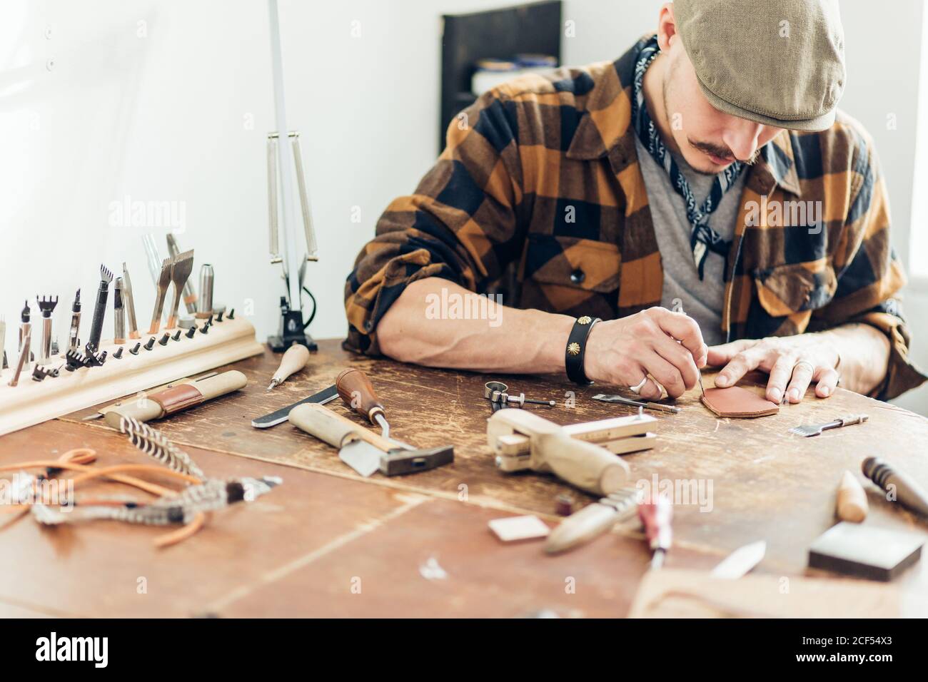 leather Crafter man dressed in plaid shirt takes tools Stock Photo