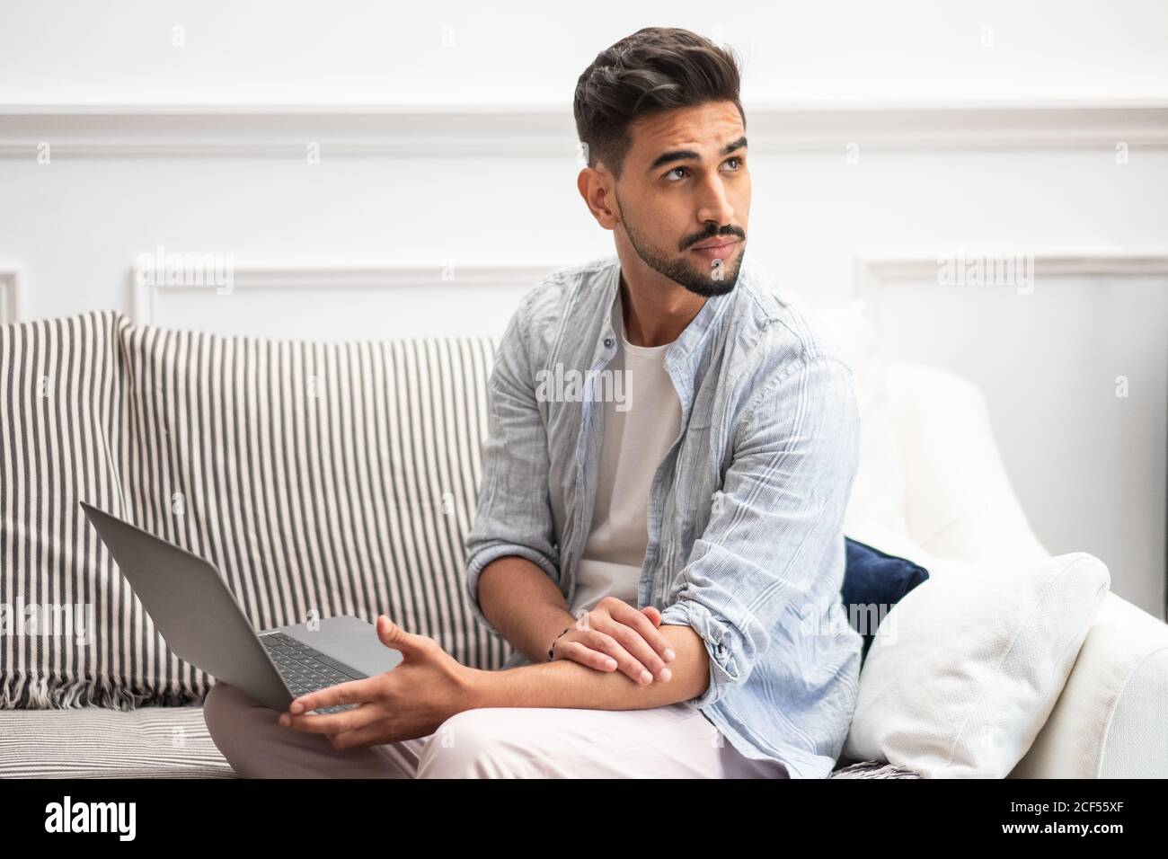 Bearded ethnic man using laptop while working on remote project at home sitting on the sofa Stock Photo