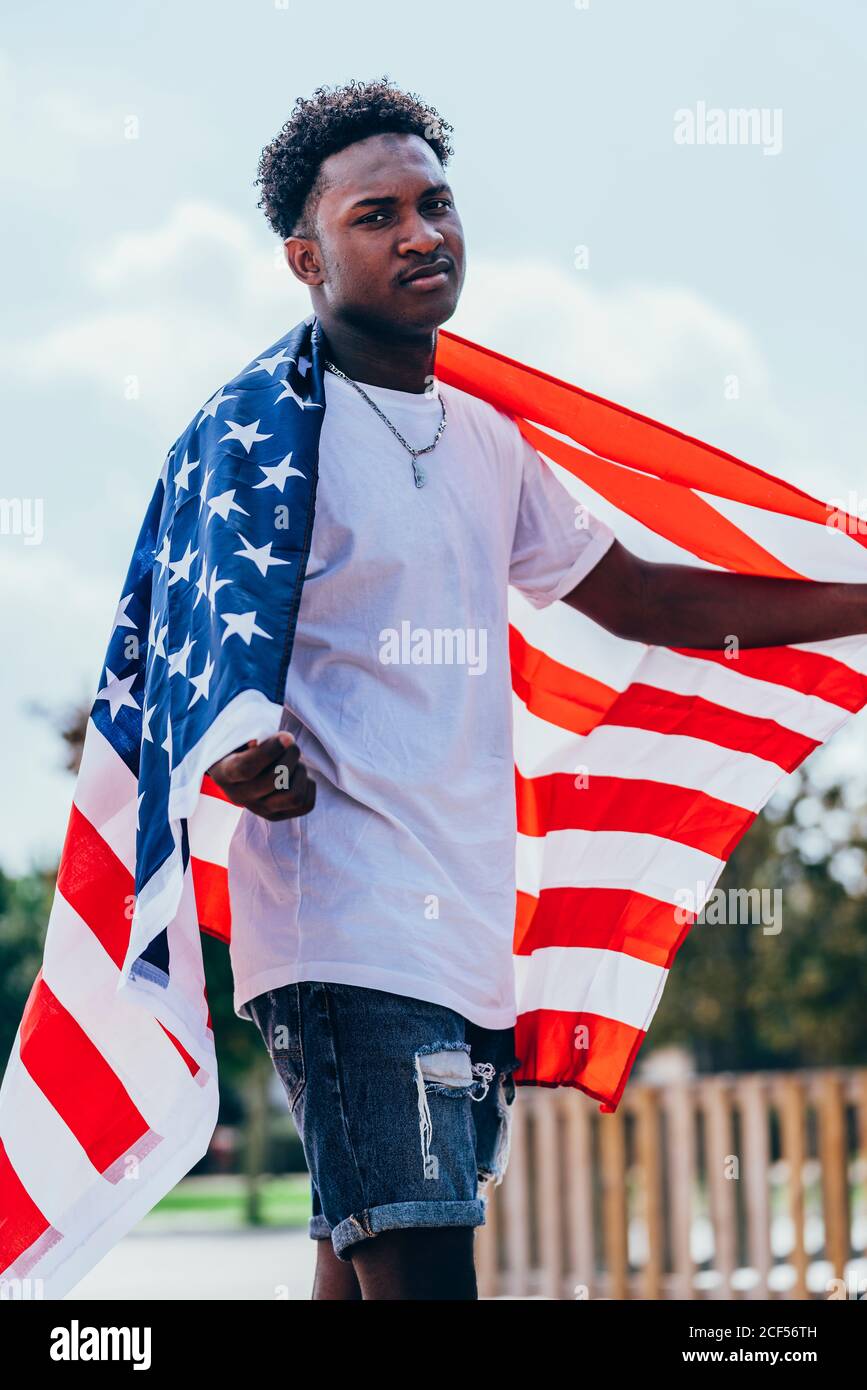 Serious African American man holding American flag on shoulder and ...