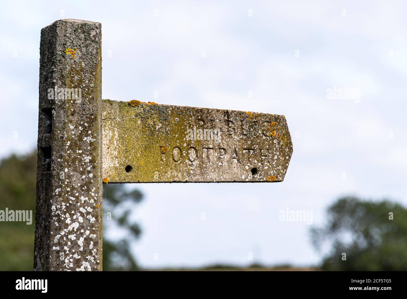 Old, vintage concrete public footpath signpost in Great Wakering, near Southend, Essex, UK. Covered in green lichen and algae. Decaying Stock Photo