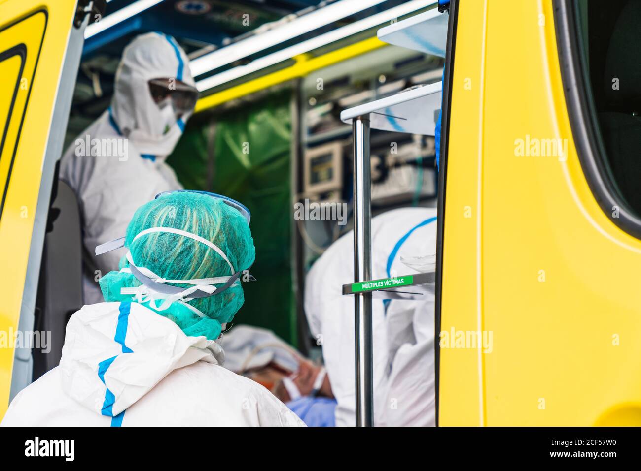 Side view of anonymous doctors in protective suit standing in ambulance car near opened door with equipment and examining patient with virus infection Stock Photo