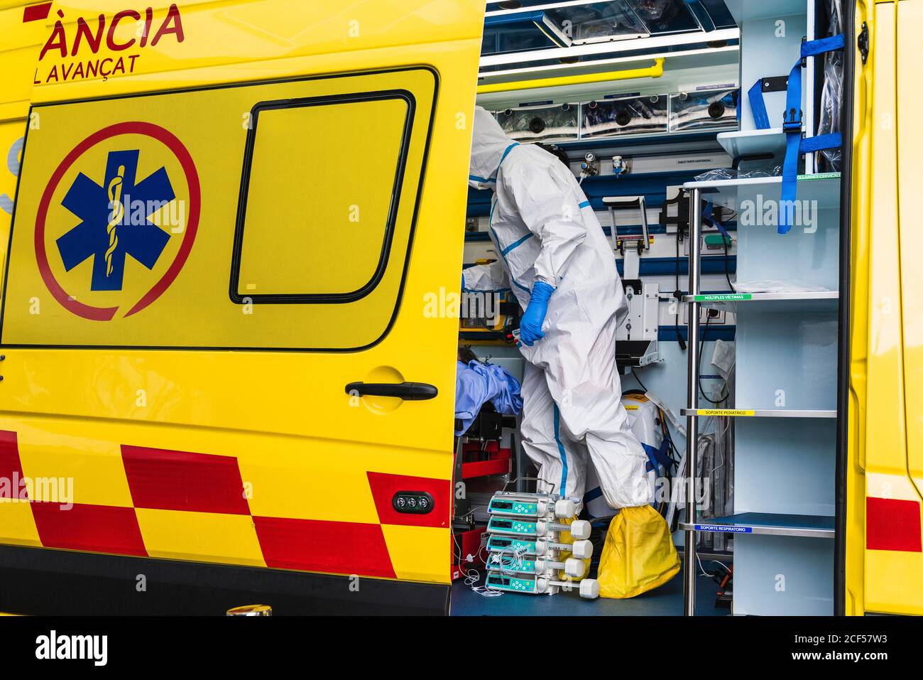 Side view of anonymous doctor in protective suit standing in ambulance car near opened door with equipment and examining patient with virus infection Stock Photo