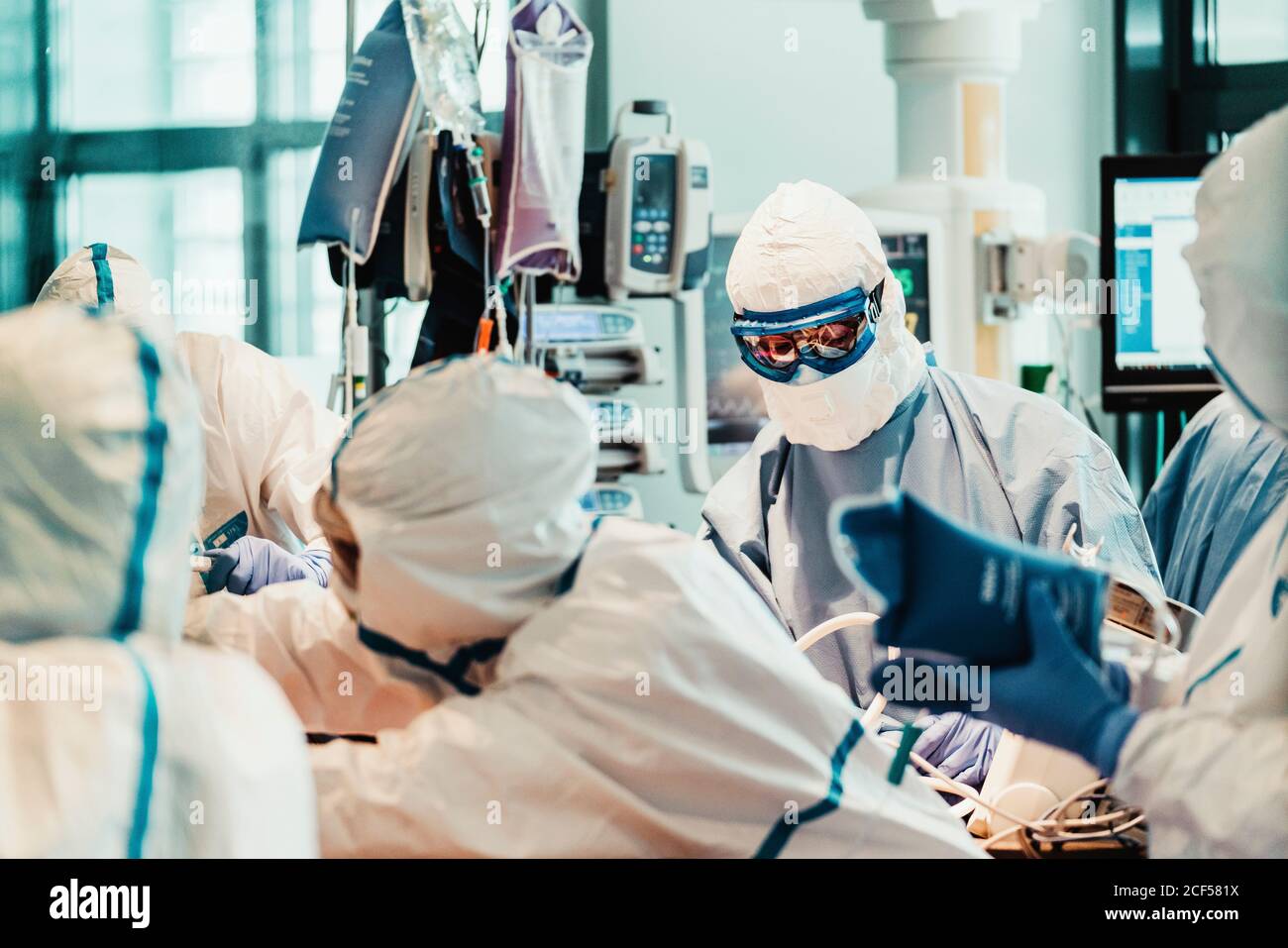 Group of professional doctors wearing protective masks and suits standing near operating table with equipment and preparing for operation in modern clinic Stock Photo