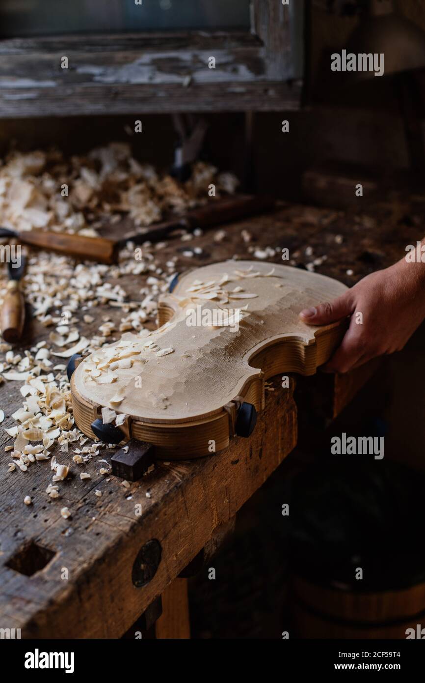 High angle of unrecognizable craftsman planing wooden violin soundboard using tool at table in work studio Stock Photo