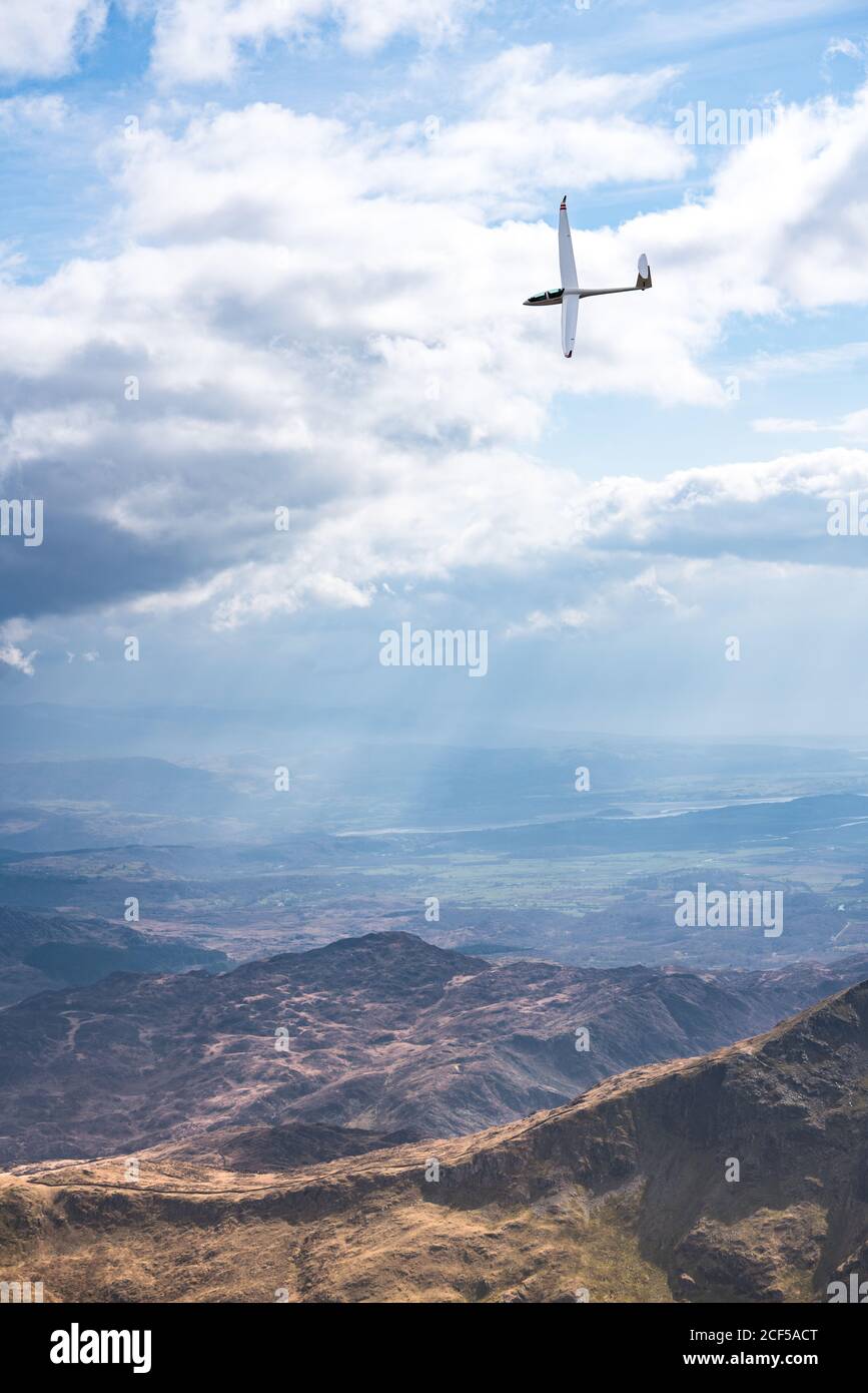 Small glider plane flying over rocky mountains in cloudy sky in summer sunny day in Wales Stock Photo