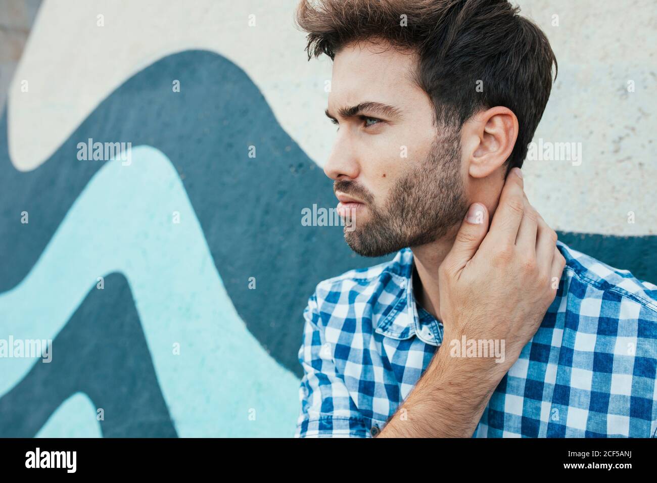 Cheerful young male in casual plaid shirt looking away with painted wall on background Stock Photo