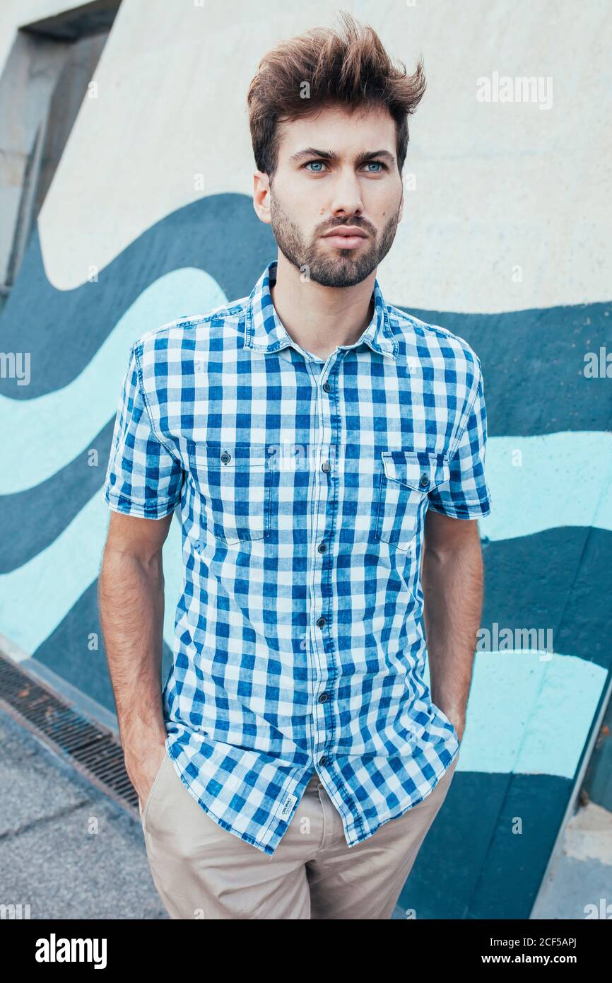 Cheerful young male in casual plaid shirt looking away with painted wall on background Stock Photo