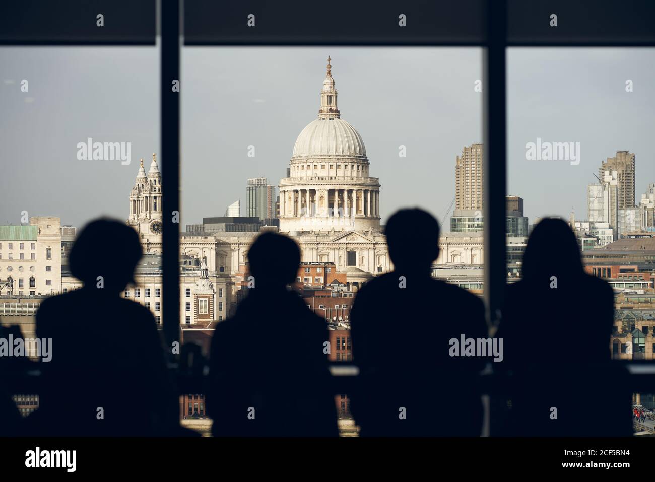 Back view silhouettes of travelers standing near window at viewpoint and admiring view of Saint Paul Cathedral in London Stock Photo