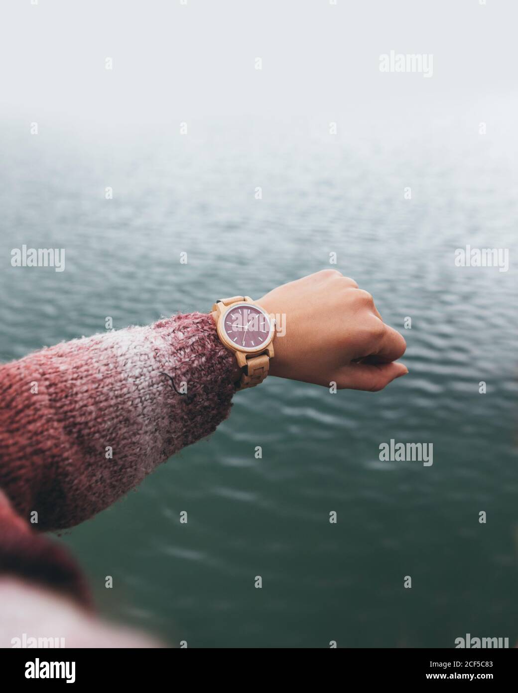 From above crop anonymous female in warm sweater checking time on stylish wristwatch while holding hand over river in cloudy day Stock Photo