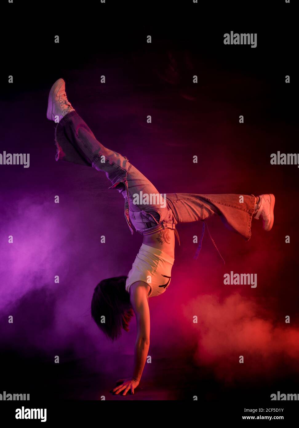 Modern female performing break dance on floor in purple and red smoke