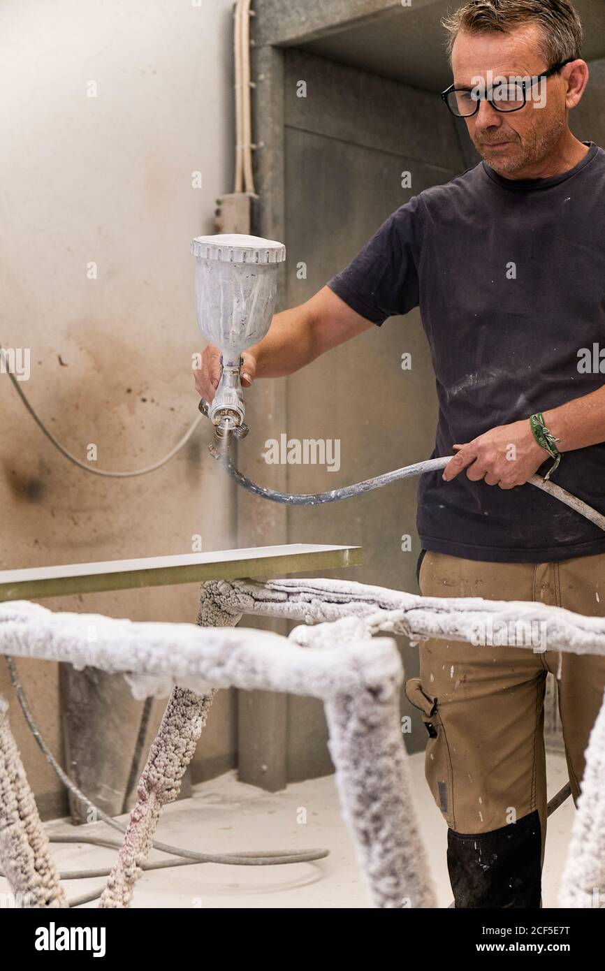 Focused workman using airbrush for applying flame retardant to wood detail ensuring fire protection in carpentry workshop Stock Photo