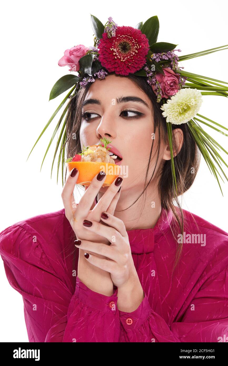 Young gorgeous Woman with wreath of colorful flowers on head looking away while holding dish in orange zest isolated on white background Stock Photo