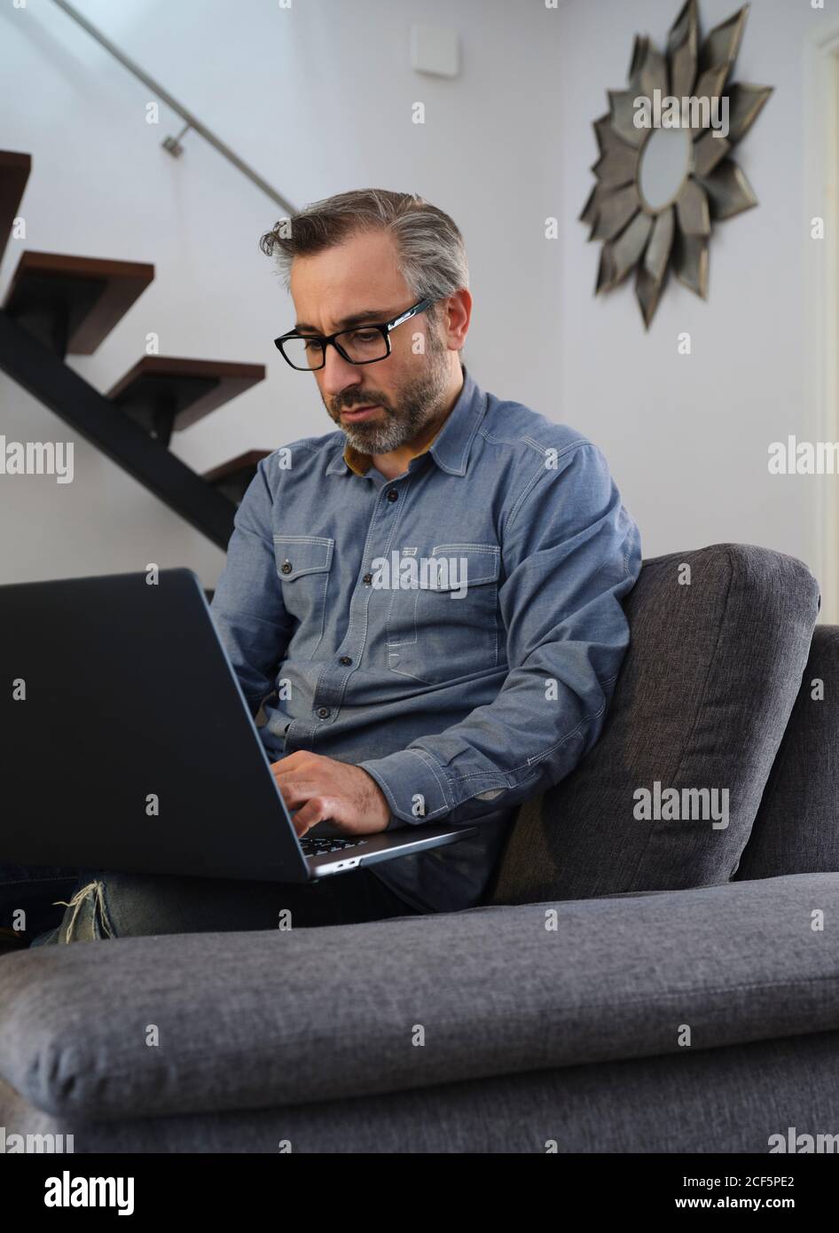 Serious man using laptop surfing the internet alone on the couch in the living room at home Stock Photo