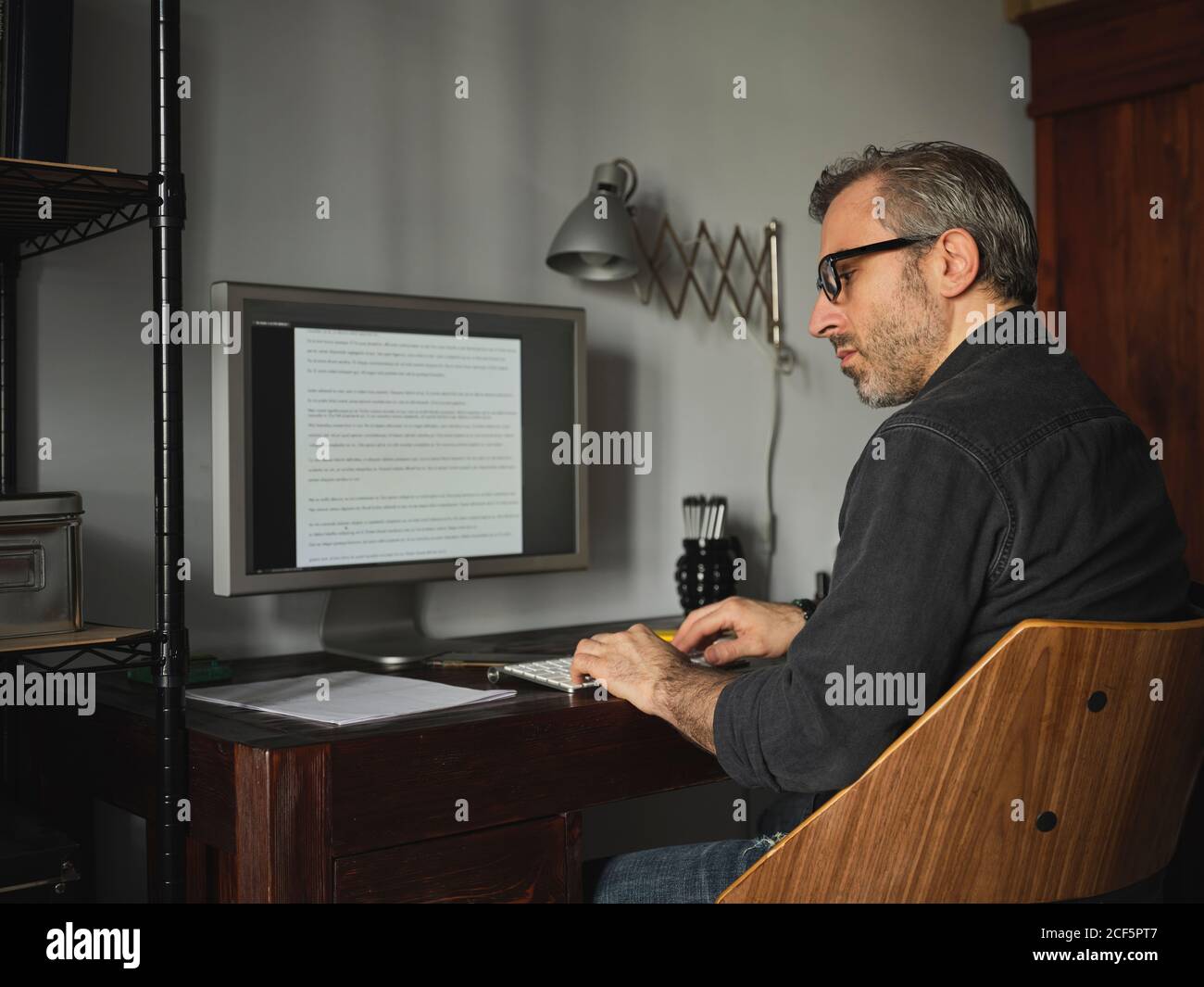man working at home desk with computer via internet typing on computer and using mouse Stock Photo