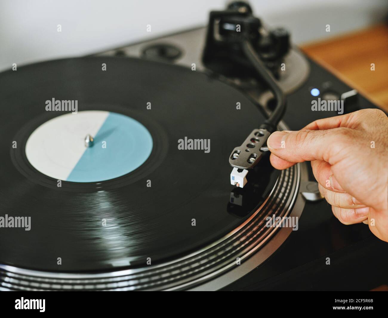From above cropped person hands adjusting a contemporary vinyl record player with retro disc placed on wooden table Stock Photo