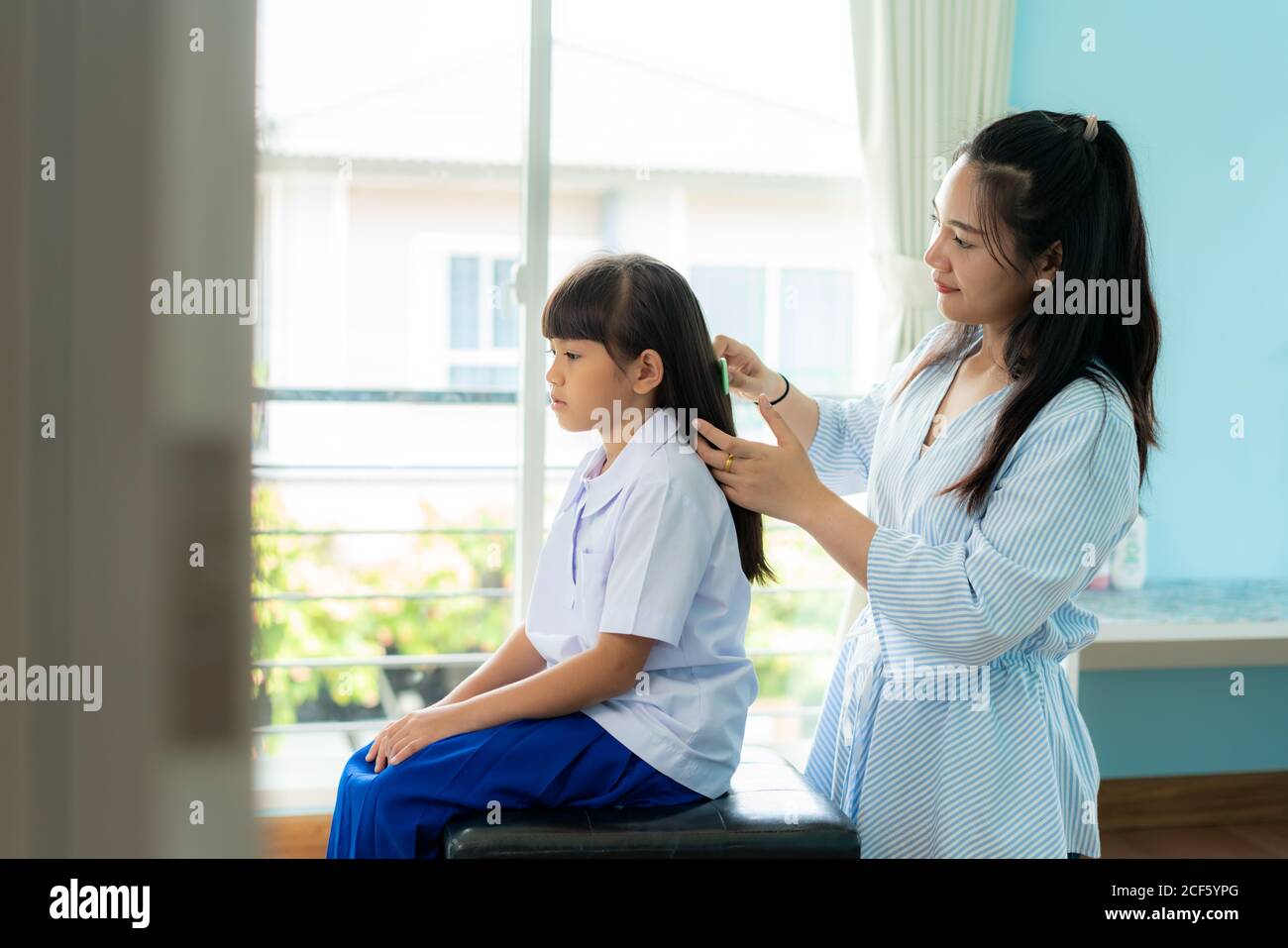 Asian Mother is combing her daughter's hair on the morning before going to school in living room at home. The morning school routine for day in the li Stock Photo