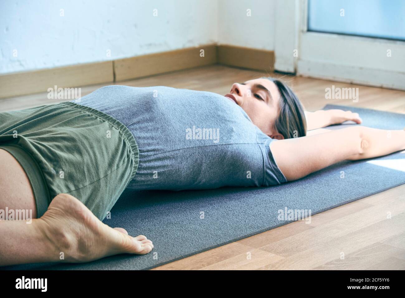 Flexible young female in sportswear lying on mat in reclined hero pose while doing yoga on floor in gym Stock Photo