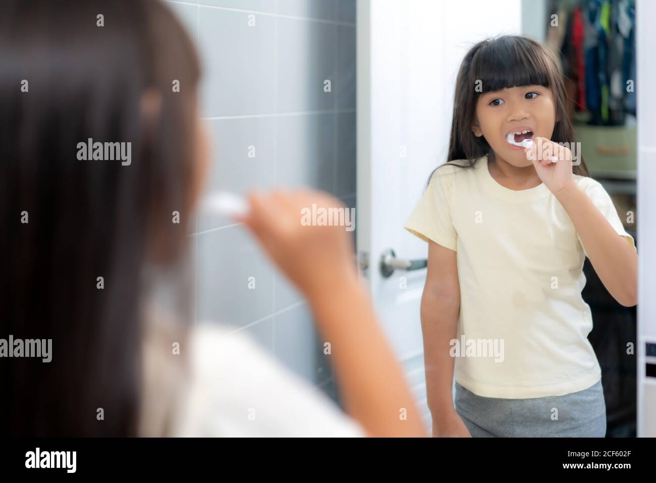 Cute Asian primary school girl brushing teeth and looking in mirror in bathroom at home. The morning school routine for day in the life getting ready Stock Photo