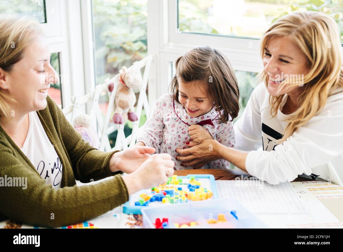 Middle aged Woman with little girl and adult daughter having fun and  playing board game while laughing and tickling each other at table Stock  Photo - Alamy