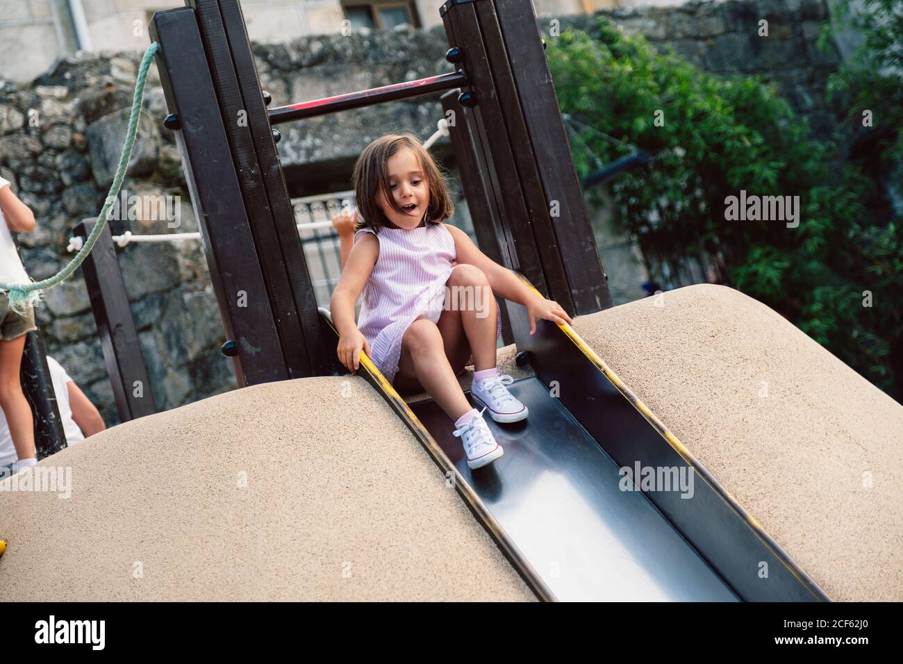 Active child holding grab rails and rolling off slide on playground in