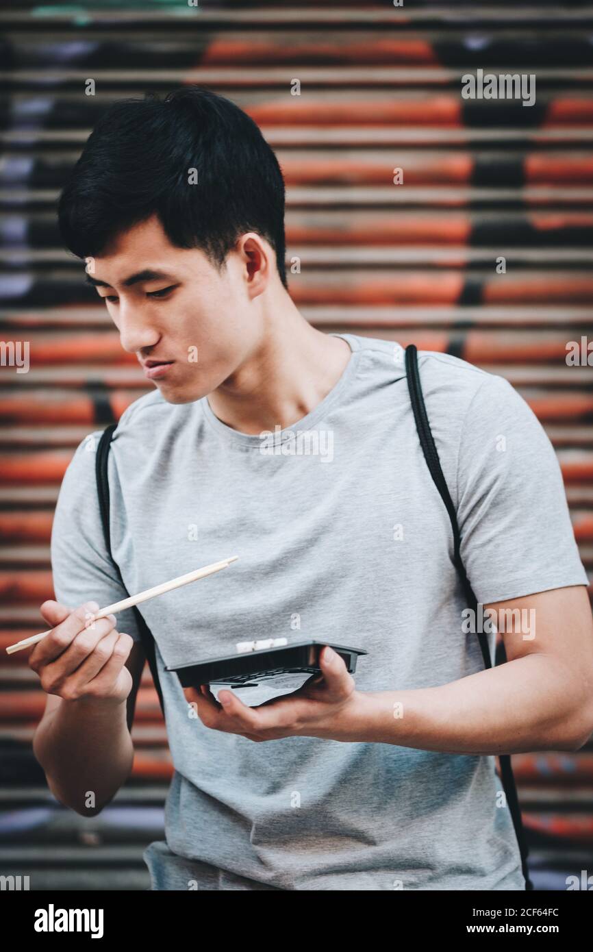 Handsome ethnic asian man eating takeaway food while standing by food