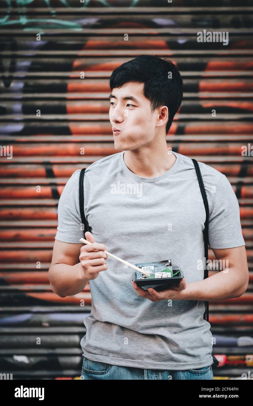 Handsome ethnic asian man eating takeaway food while standing by food