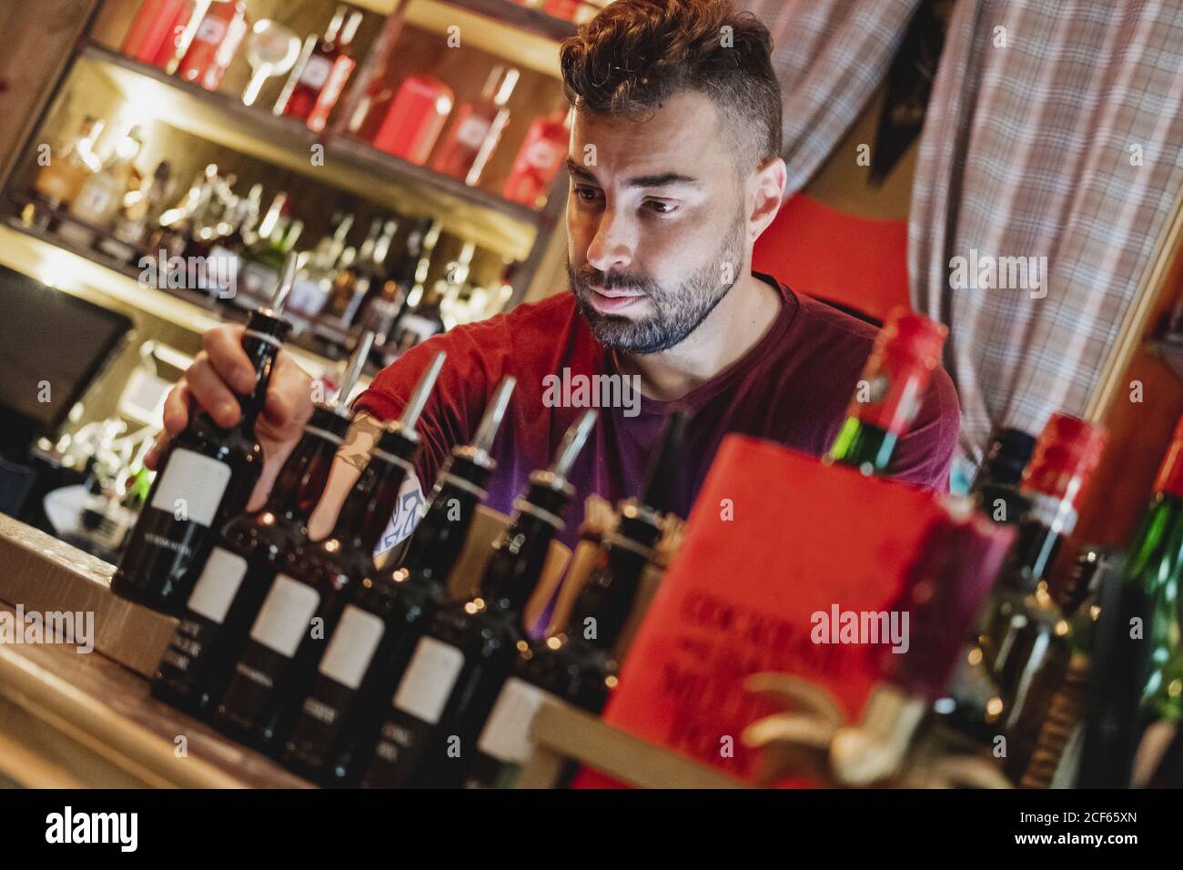 Barman in uniform and red gloves preparing cocktail and pouring drink to red bottle for mixing Stock Photo