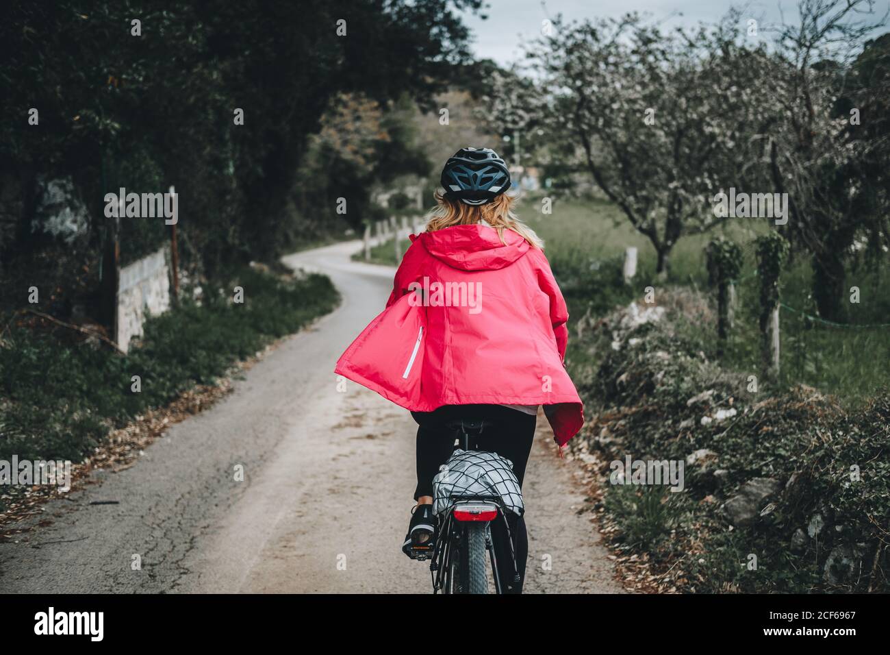 Back view of anonymous woman while cycling on countryside road on cloudy day Stock Photo