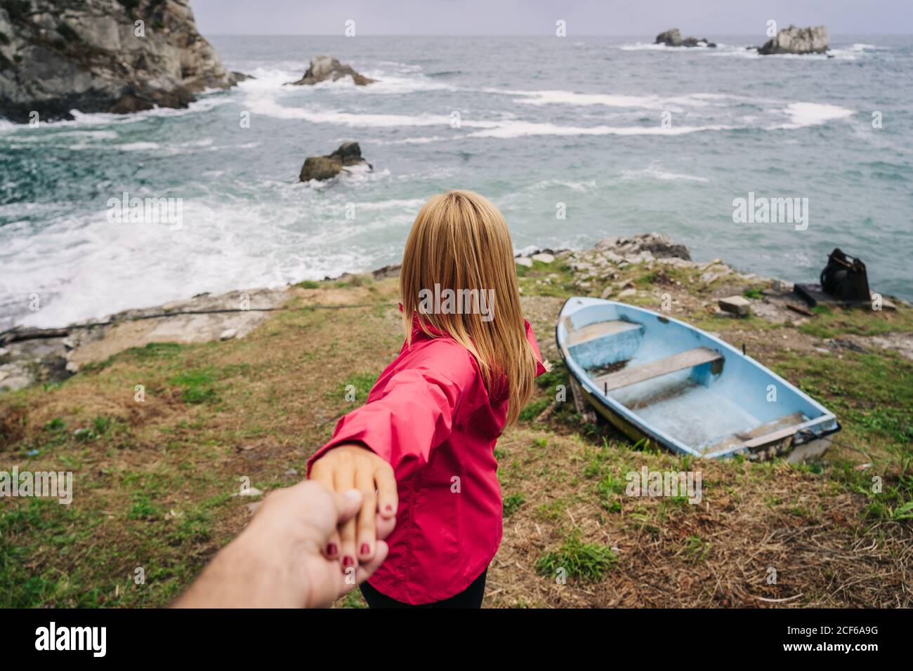 Woman holding hand of crop person inviting to follow to seashore with boat Stock Photo