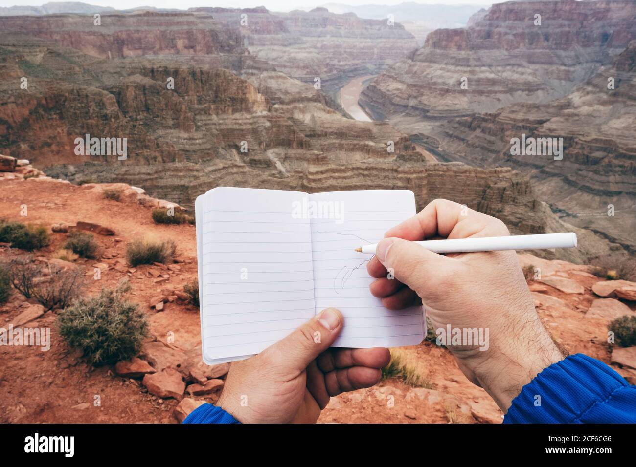 Crop man making notes in diary while having rest at edge of cliff in ...