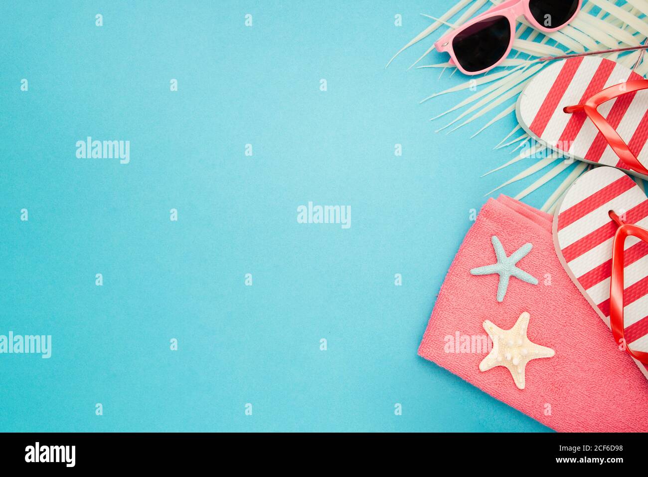 Top view composition of sunglasses and flip flops placed with beach towel on blue background with palm leaves and starfish representing summer vacation on beach Stock Photo