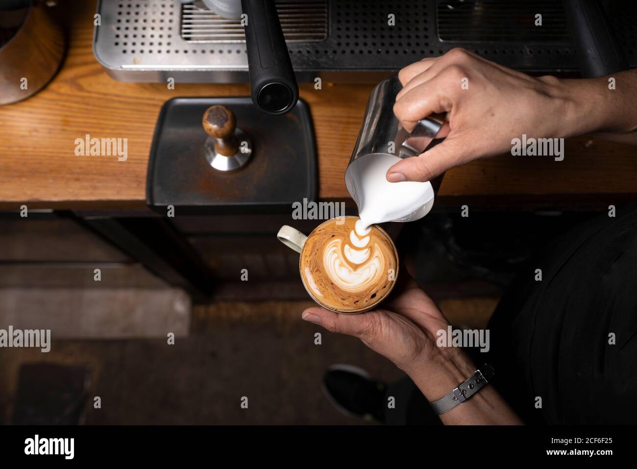 From above crop hands of professional employee preparing cappuccino with pattern on top in coffee shop Stock Photo