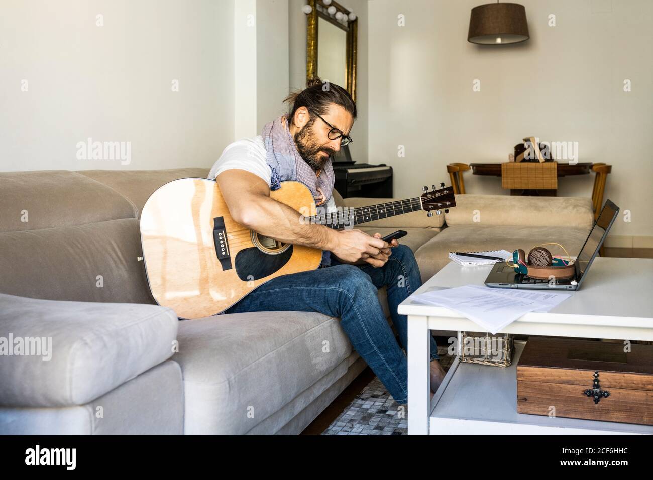 Cheerful man with guitar checking smartphone on sofa Stock Photo