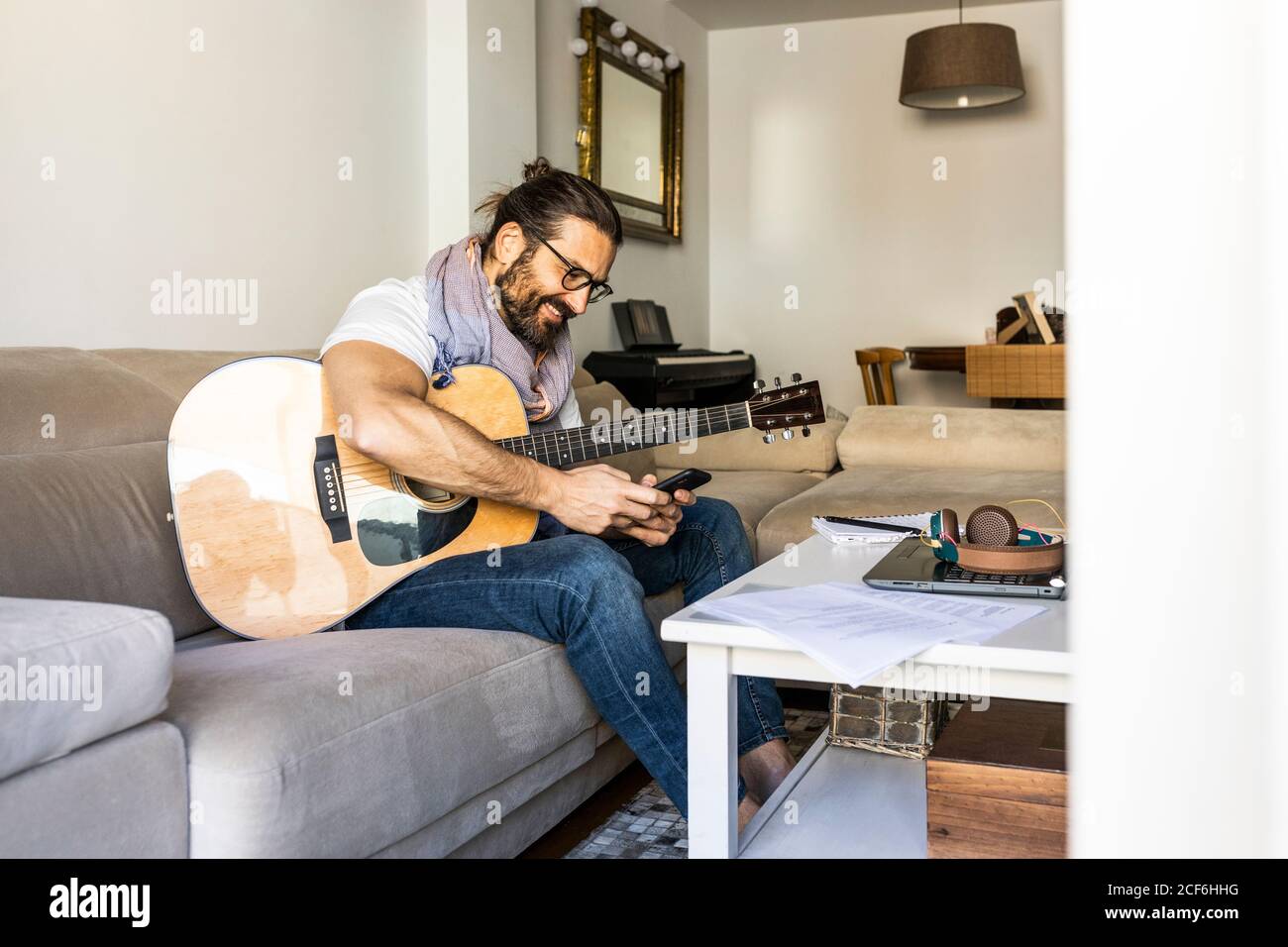 Cheerful man with guitar checking smartphone on sofa Stock Photo