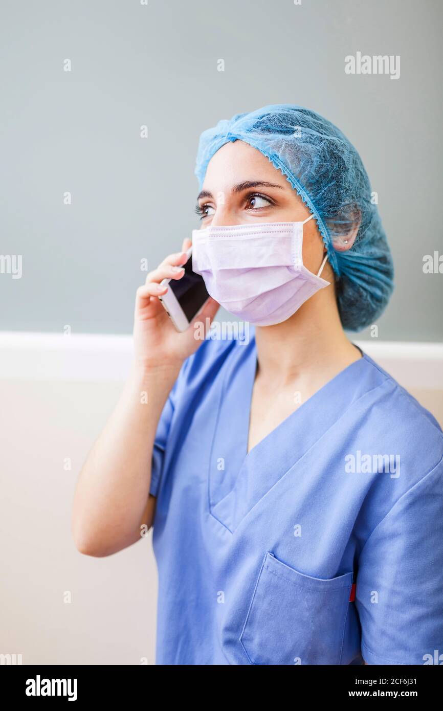 Female surgeon leaning on corridor wall while talking with her smart phone Stock Photo