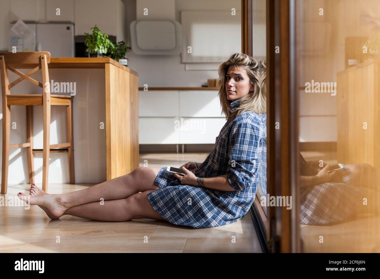 Beautiful and young Woman sitting on the floor of her house, looking at ...