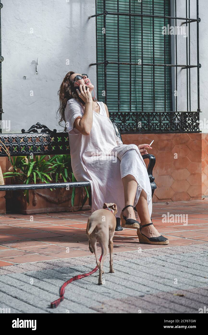 Merry positive female with cigarette calling on phone and laughing with