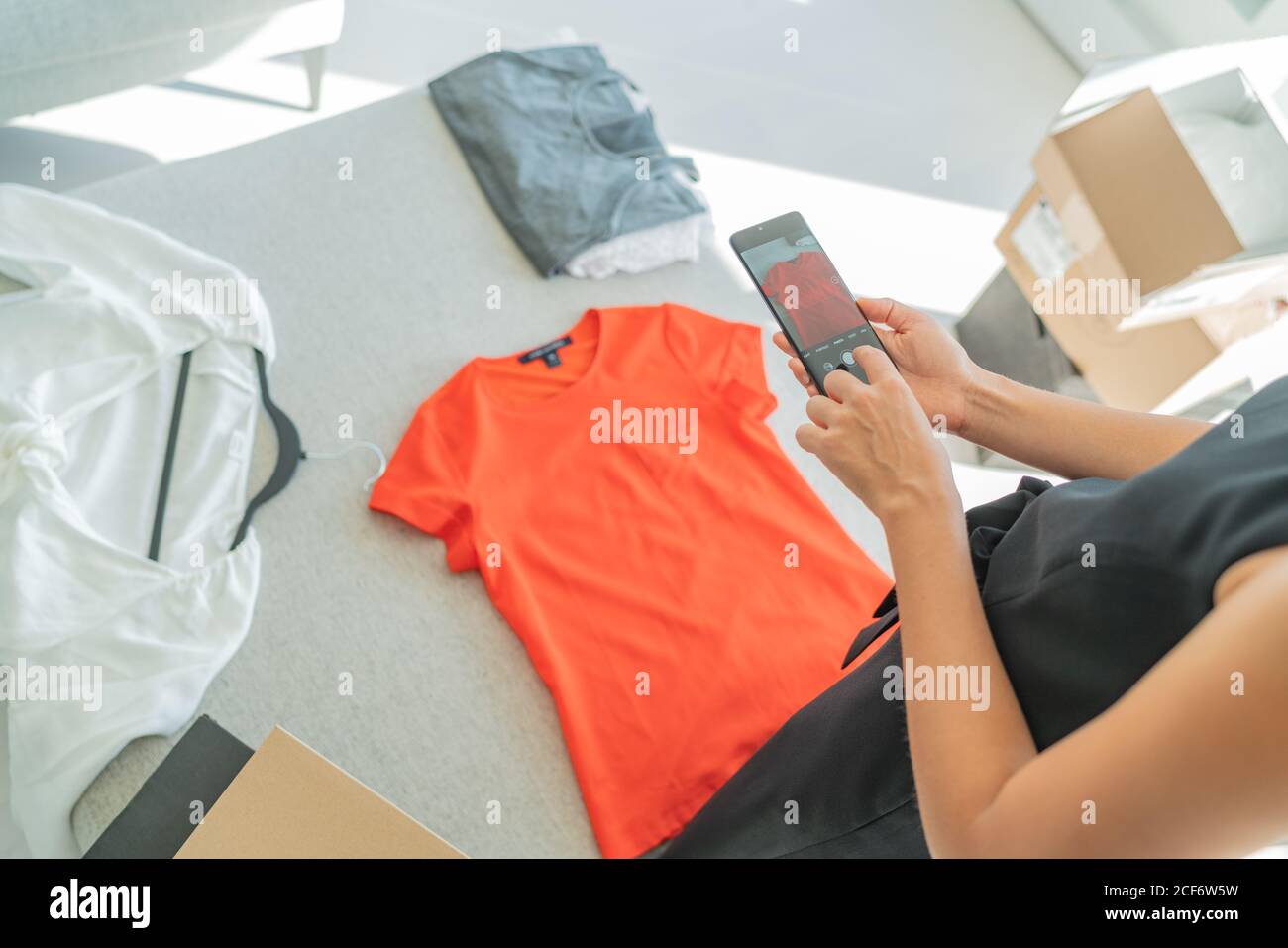 Selling online through phone app taking mobile photo of t shirt doing e-commerce small business at home Stock Photo