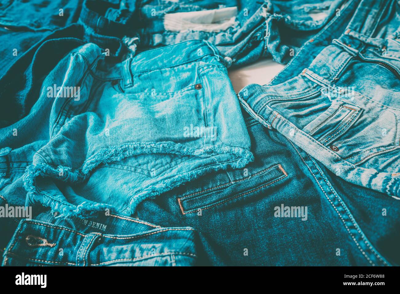 Jeans fast fashion textile industry tons of pairs of pants produced every year going to waste. Closeup of many different denim fabrics of blue indigo Stock Photo