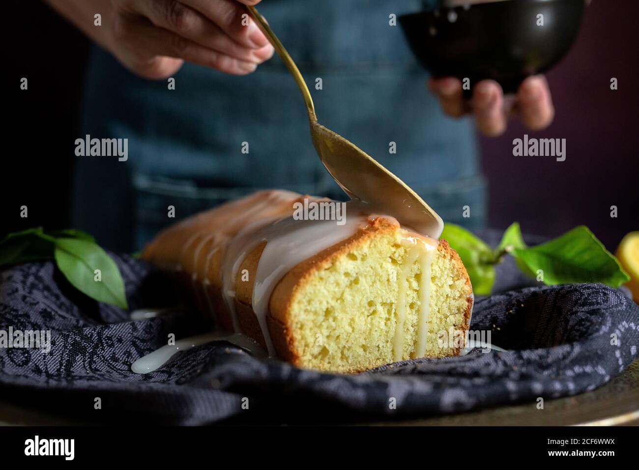 Cropped unrecognizable Woman hands pouring white sweet glaze on a homemade lemon cake Stock Photo