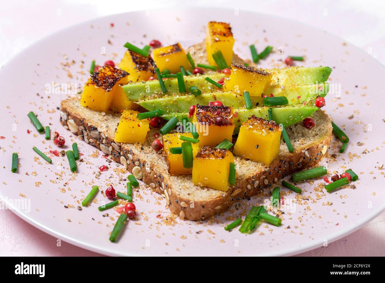 Homemade toasted bread with avocado, mango and aromatic herbs on pink background.Vegetarian food.Healthy food concept. Stock Photo