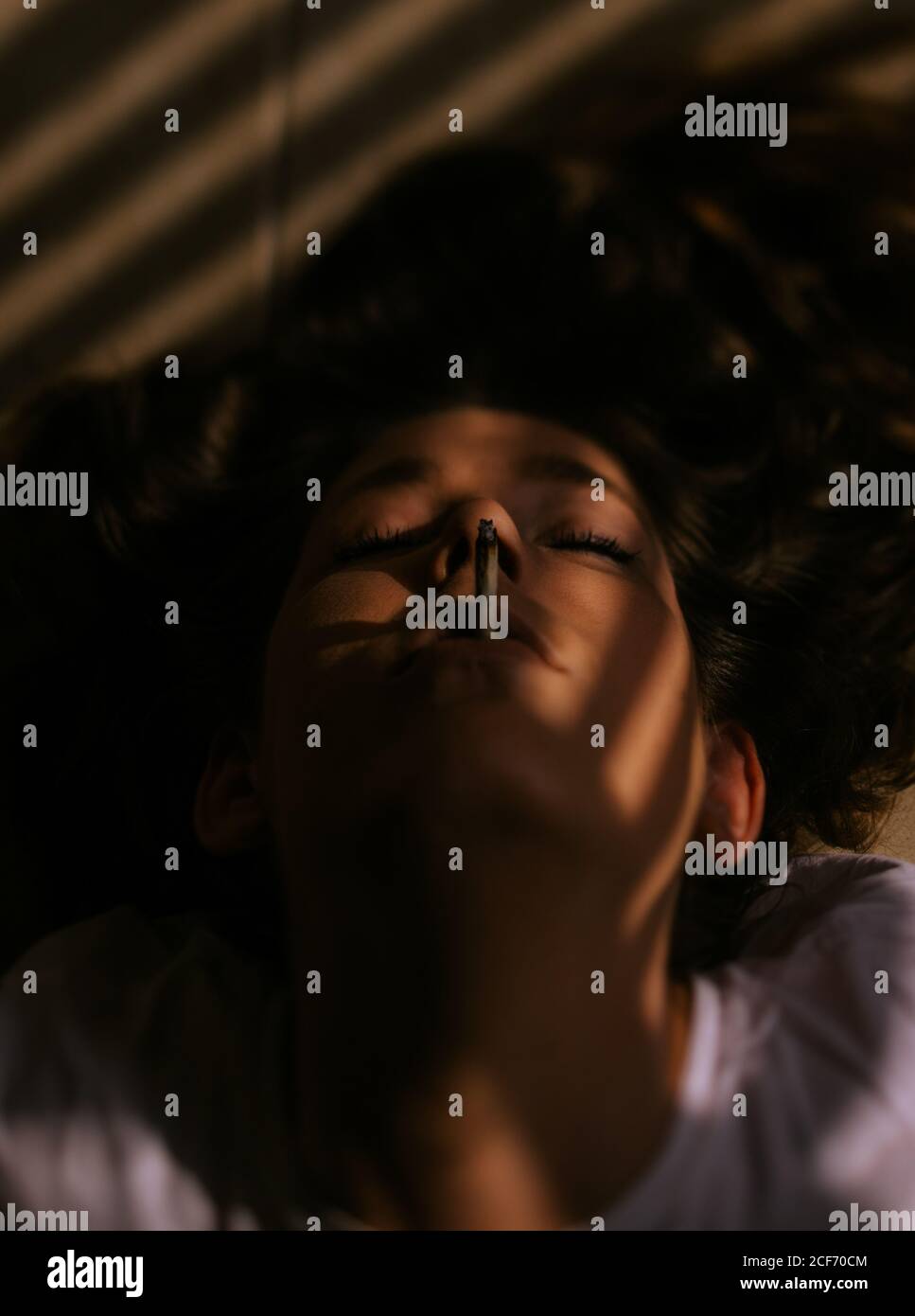 Woman lying down with closed eyes smoking cigarette Stock Photo