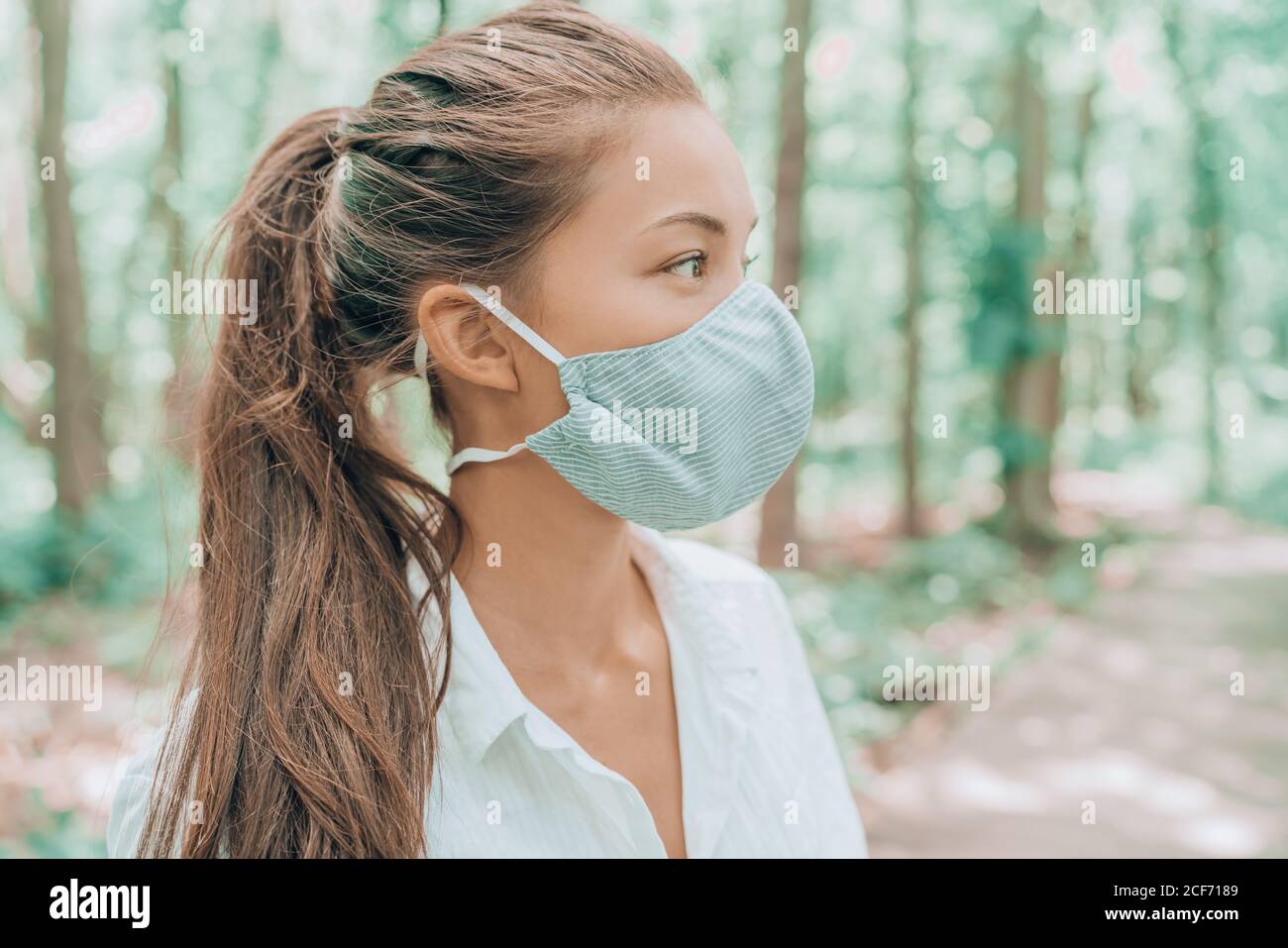 Face mask of cotton fabric are breathable for skin. Asian woman wearing corona virus mouth covering walking outdoors in woods Stock Photo