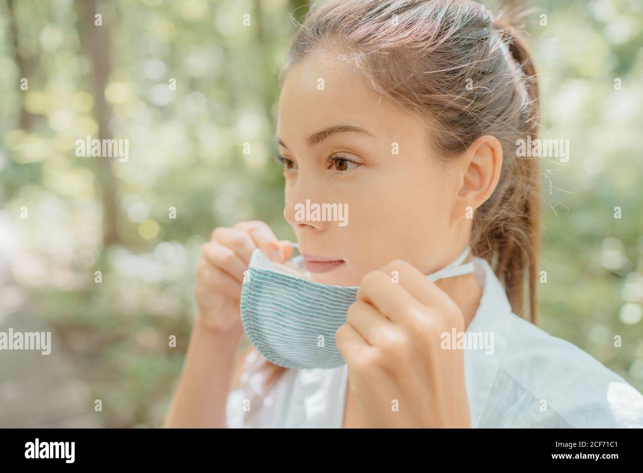 Asian beauty woman putting on mask on face. Wearing corona virus prevention masks for long hours are creating irritation, skin problems, acne pimples Stock Photo