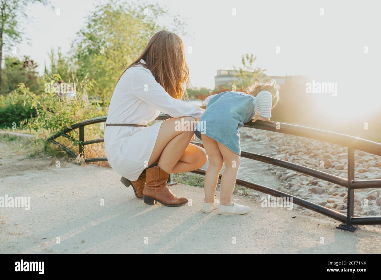Side view of young Woman and little girl bending over railing and looking at fast water stream on sunny day in park Stock Photo