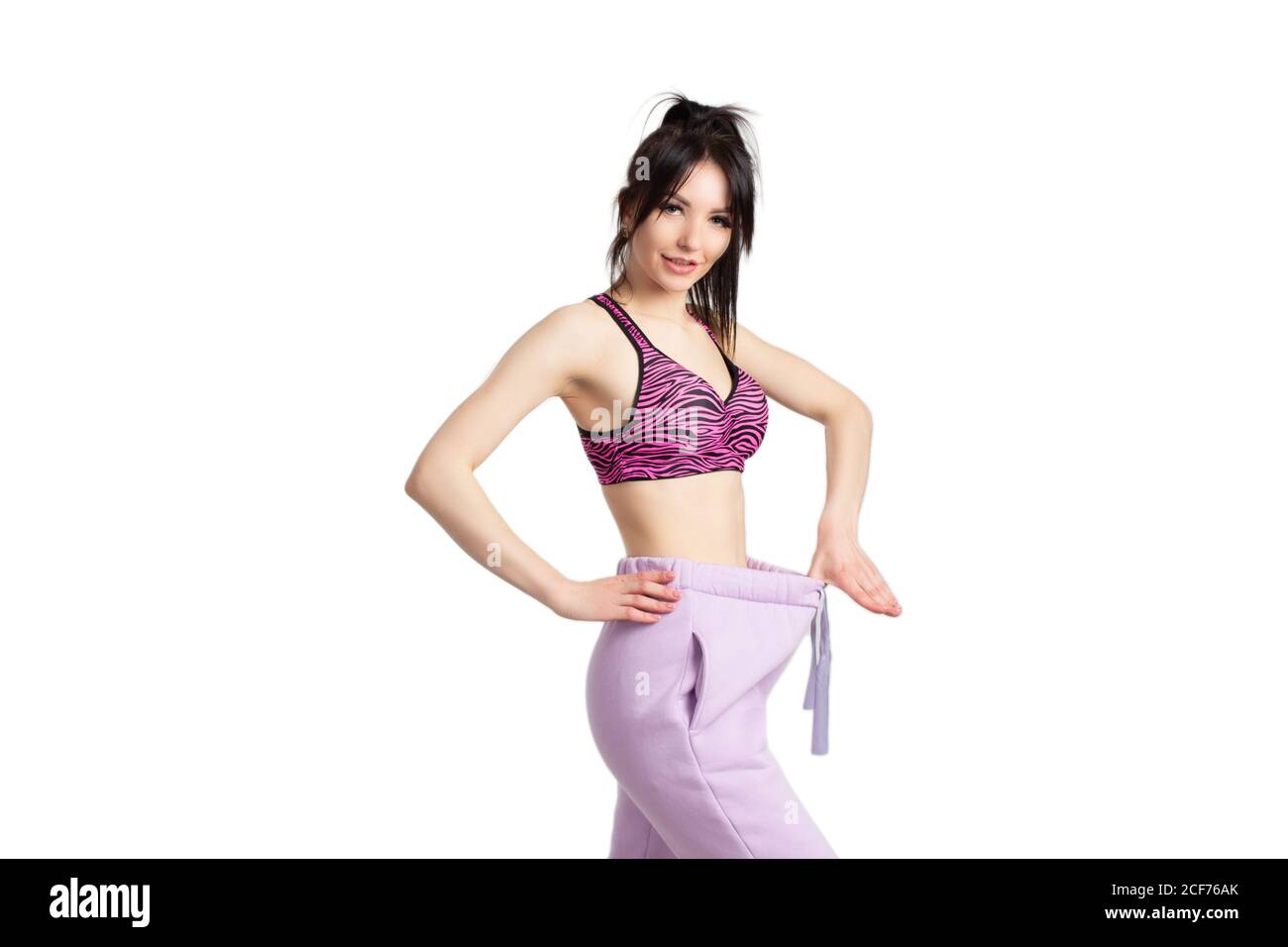 Fitness girl in sports tops tries on big, wide pants on a white background. The concept of weight loss. Stock Photo