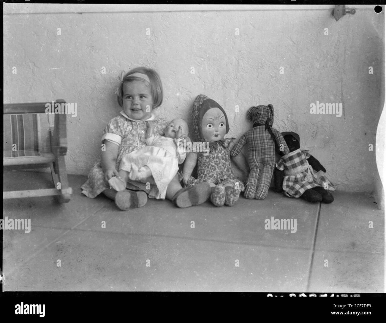 Young child with a baby doll on her lap and a rag doll, a teddy bear and a golliwog next to her, Australia, ca. 1930 . Stock Photo