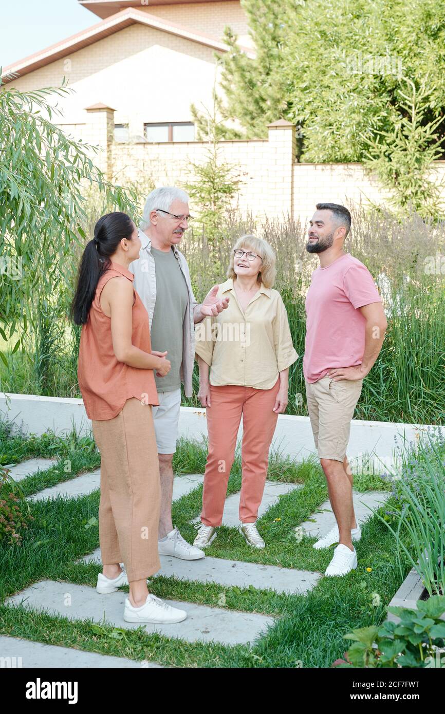 Group of seniors and young adult people standing together in backyard on summer day chatting about something, full shot Stock Photo