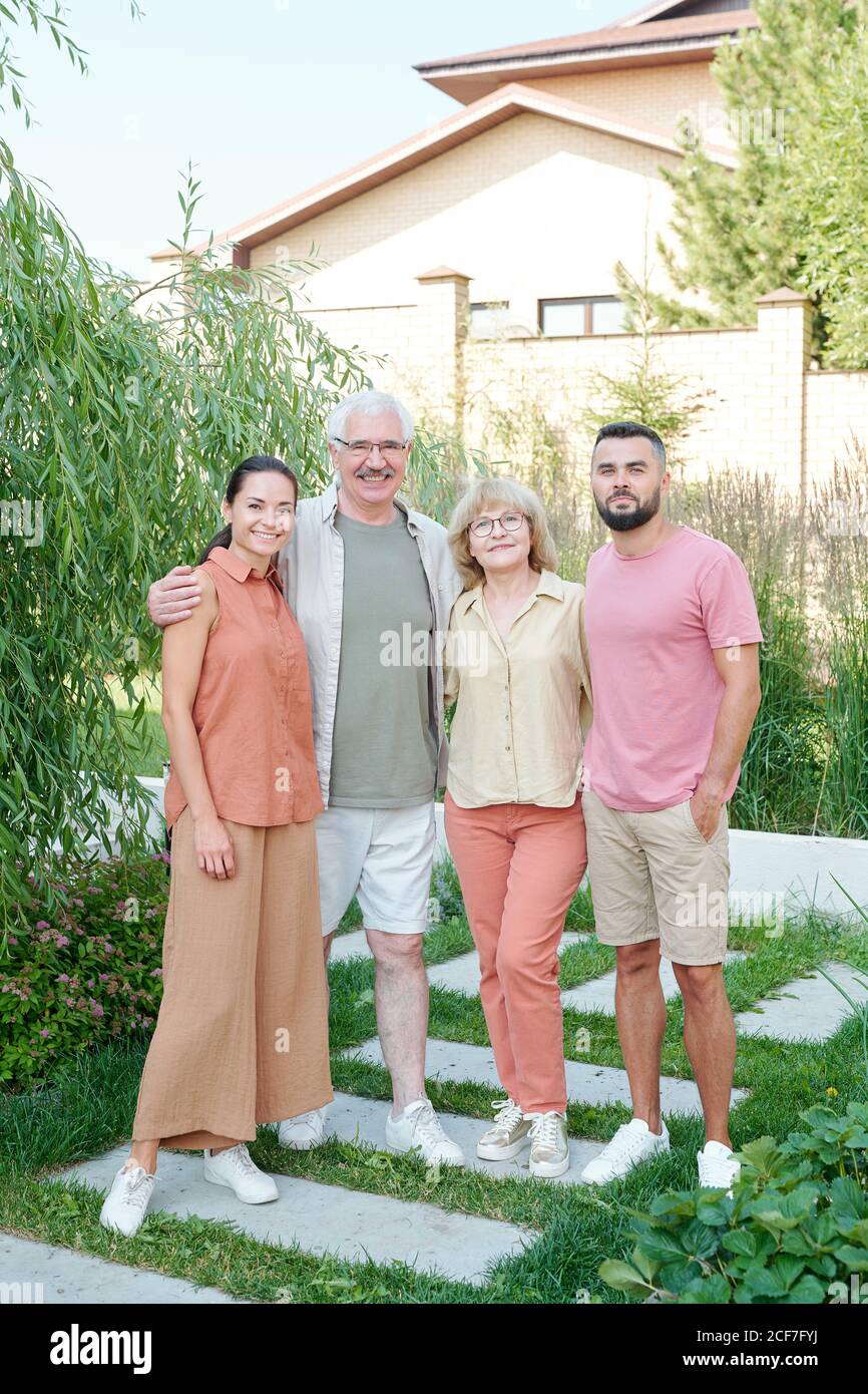 Full shot family portrait of senior parents and their young adult children standing together outdoors looking at camera Stock Photo